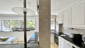 Una cocina moderna con armarios blancos, encimera negra y una estantería de vidrio para vinos.