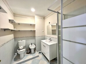 Ein modernes Badezimmer mit Toilette, Bidet und Waschbecken, inklusive einer Duschkabine aus Glas und einem Spiegel über dem Waschbecken.