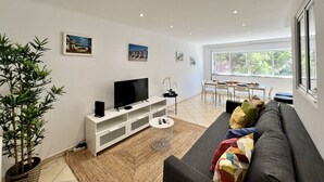 Una sala moderna con televisor de pantalla plana, un sofá, una mesa de comedor con sillas y un ventanal con vistas a zonas verdes.