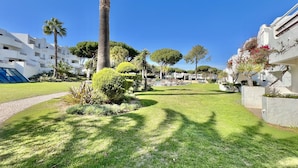A well-maintained garden with palm trees and manicured lawns, surrounded by modern buildings with balconies. - Albufeira Balaia Golf Village 2 (Albufeira)