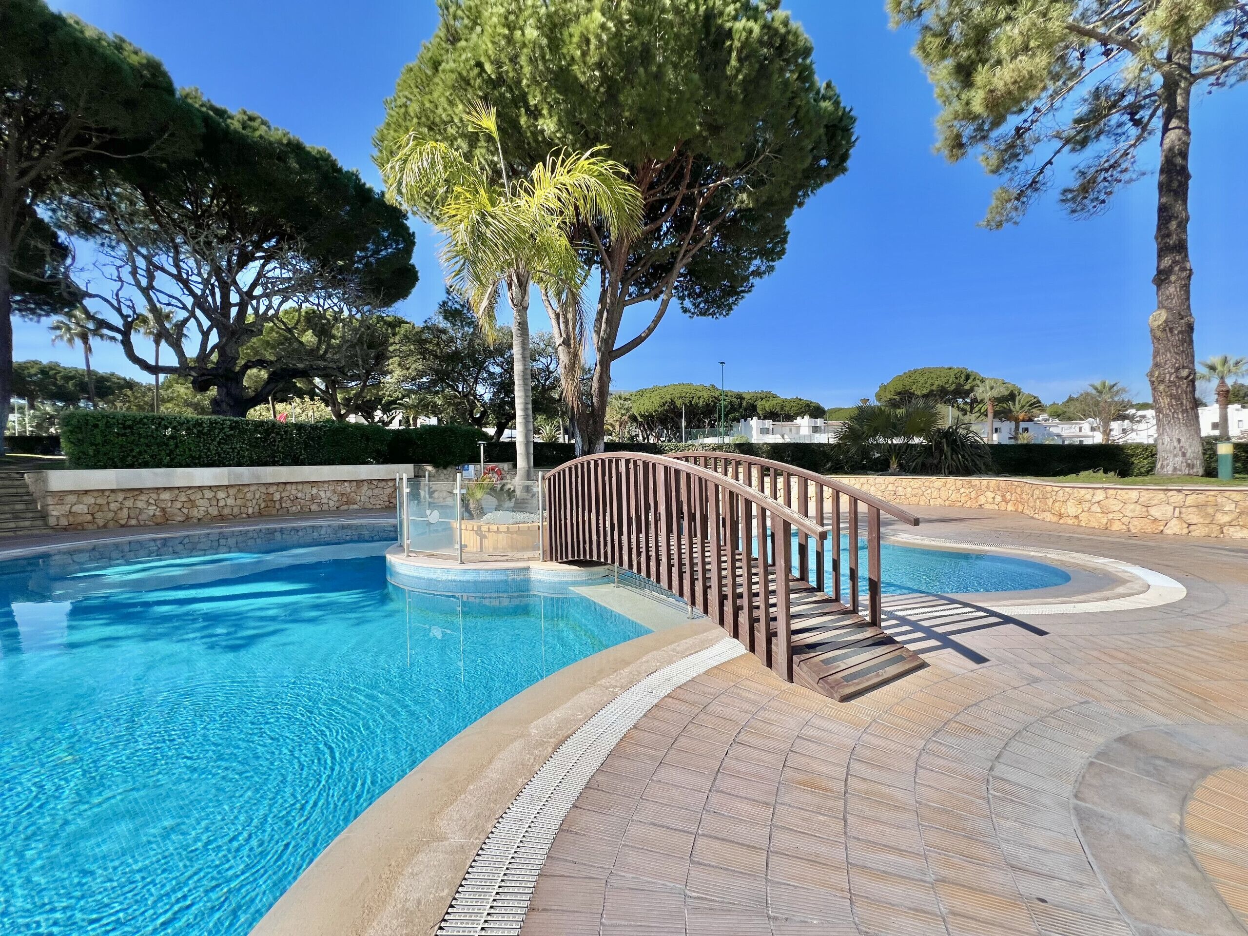 A swimming pool with a wooden deck and a stone wall.