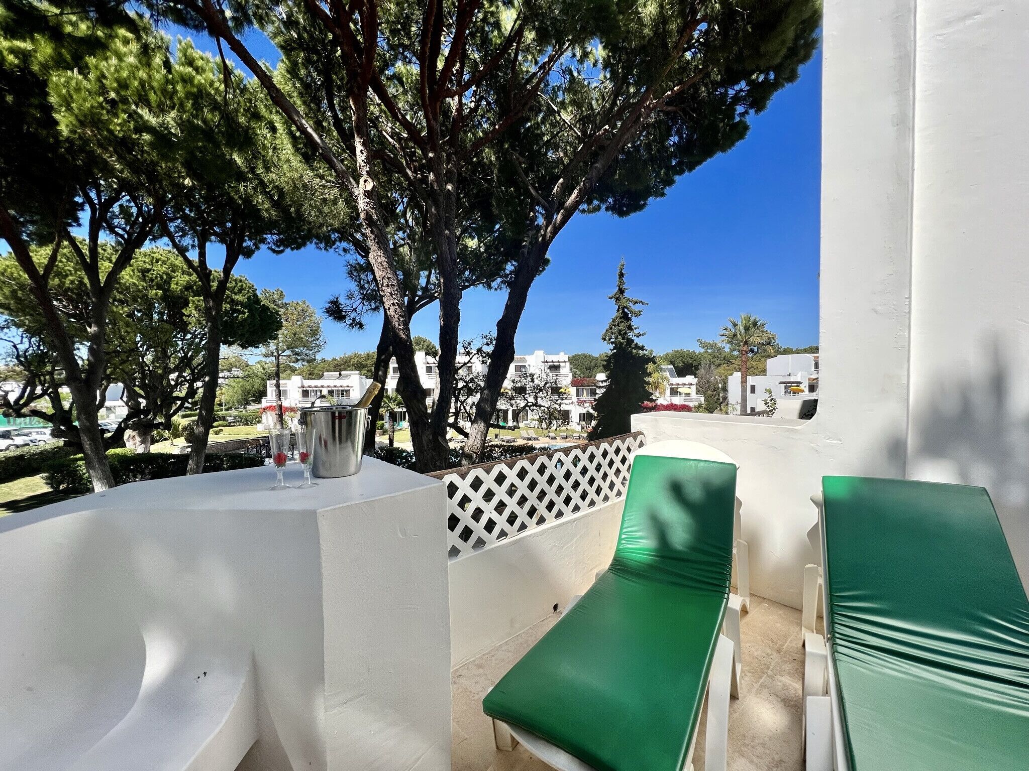 A terrace with a white wall, a green cushioned lounge chair, and a metal bucket with a glass.