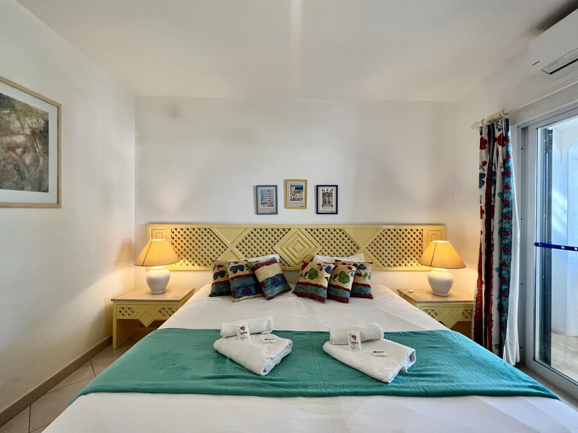 Habitación de hotel con cama, dos mesitas de noche con lámparas, colcha verde y una ventana con cortinas.