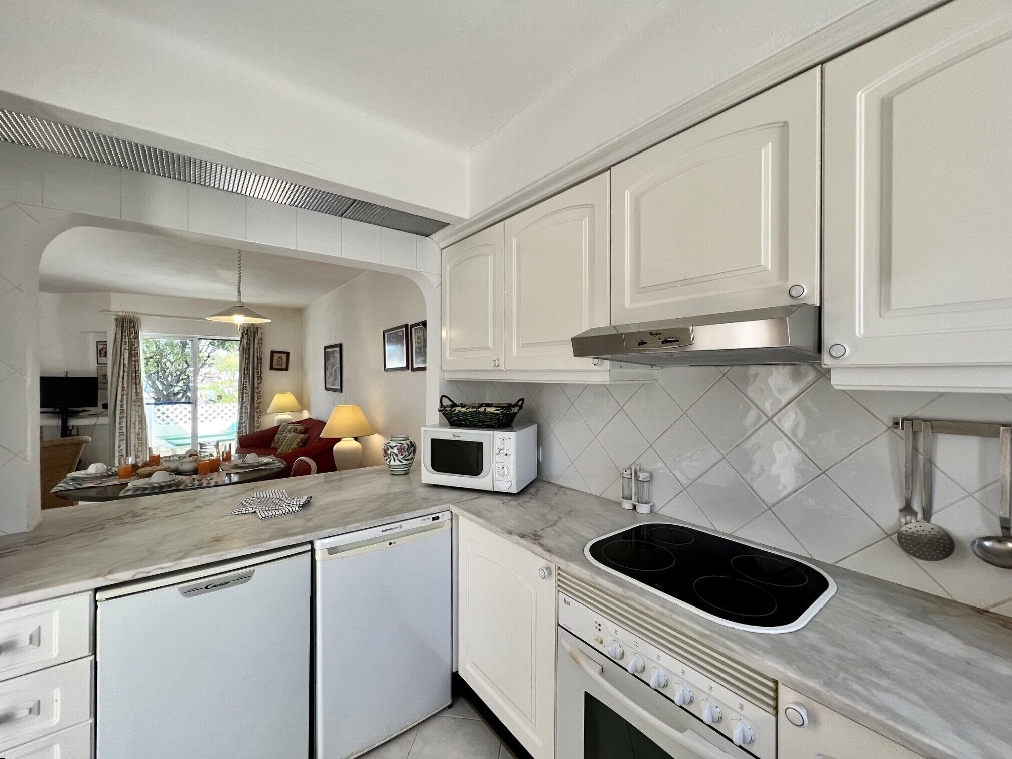 Una cocina compacta con armarios blancos, microondas, lavavajillas y estufa.