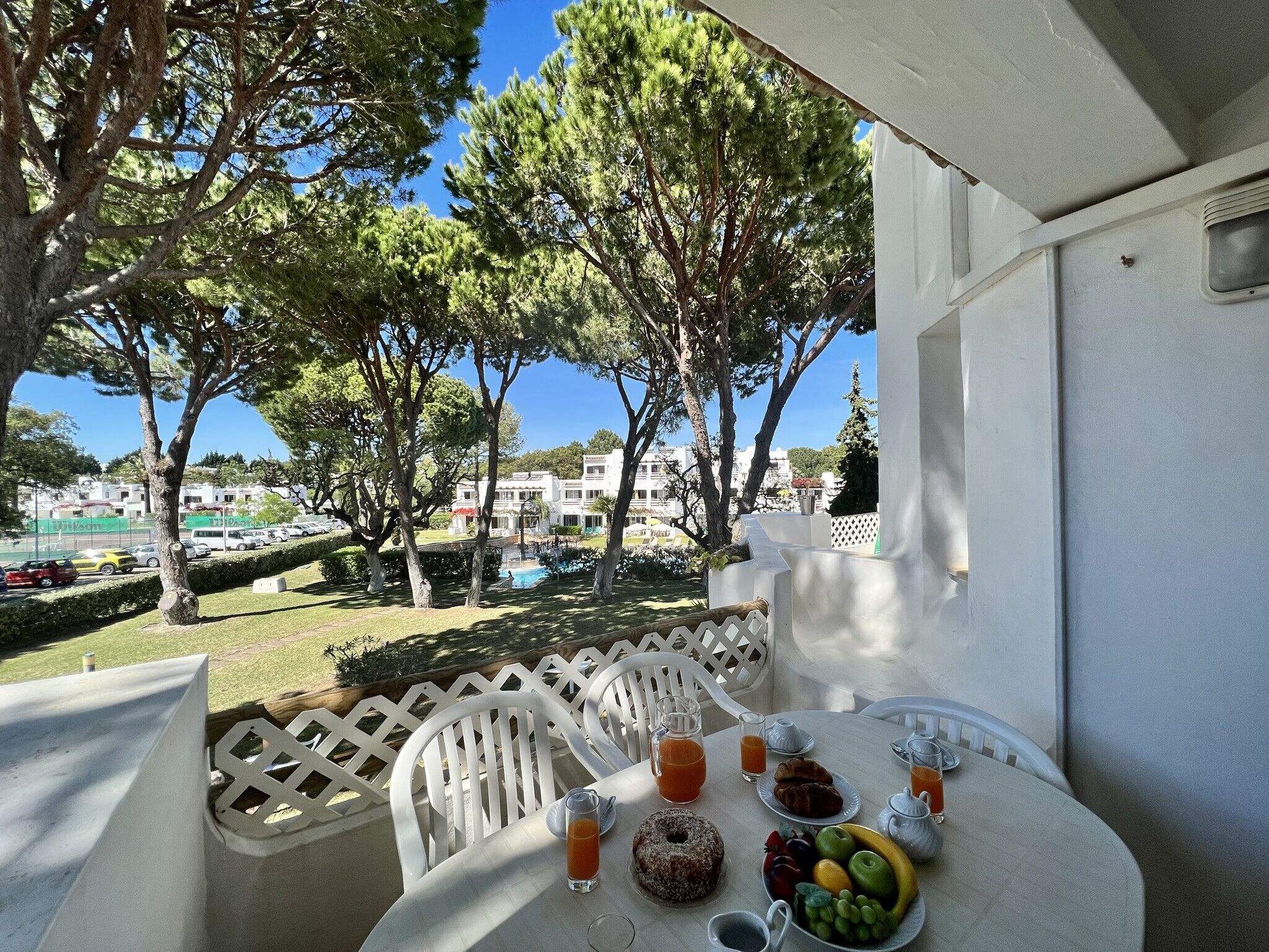 A balcony with a table set for breakfast, overlooking a pool and buildings.