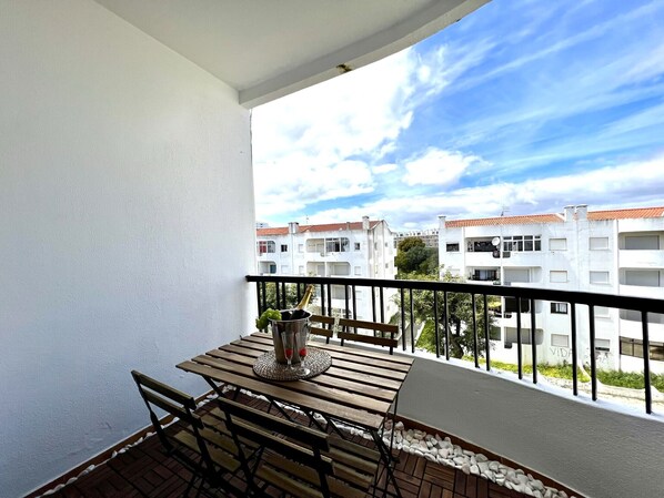 A balcony with a table and chairs, a bottle of champagne, and a view of white buildings with red roofs.