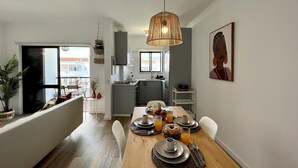 Un comedor moderno con una mesa de madera dispuesta para el desayuno, una lámpara colgante y vistas a la cocina y al balcón.