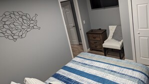 A bedroom with a bed, a chair, a dresser, a TV, and a wall art piece. - The Calico Cottage - Fire Pit - Hot Tub (Lewis Center)