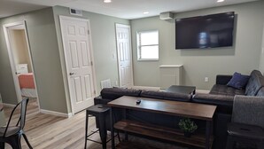 A modern living room with a sectional sofa, a wooden coffee table, and a flat-screen TV mounted on the wall. - The Calico Cottage - Fire Pit - Hot Tub (Lewis Center)
