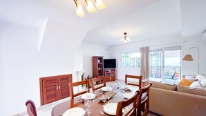 A dining area with a round table set for four, a sofa, and a TV in the background.