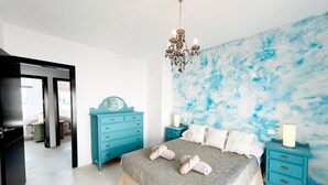 A bedroom with a bed, a dresser, a nightstand, a chandelier, and a blue abstract wall.