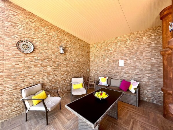 A room with a stone wall, a round table with a fruit bowl, two sofas, and two chairs.