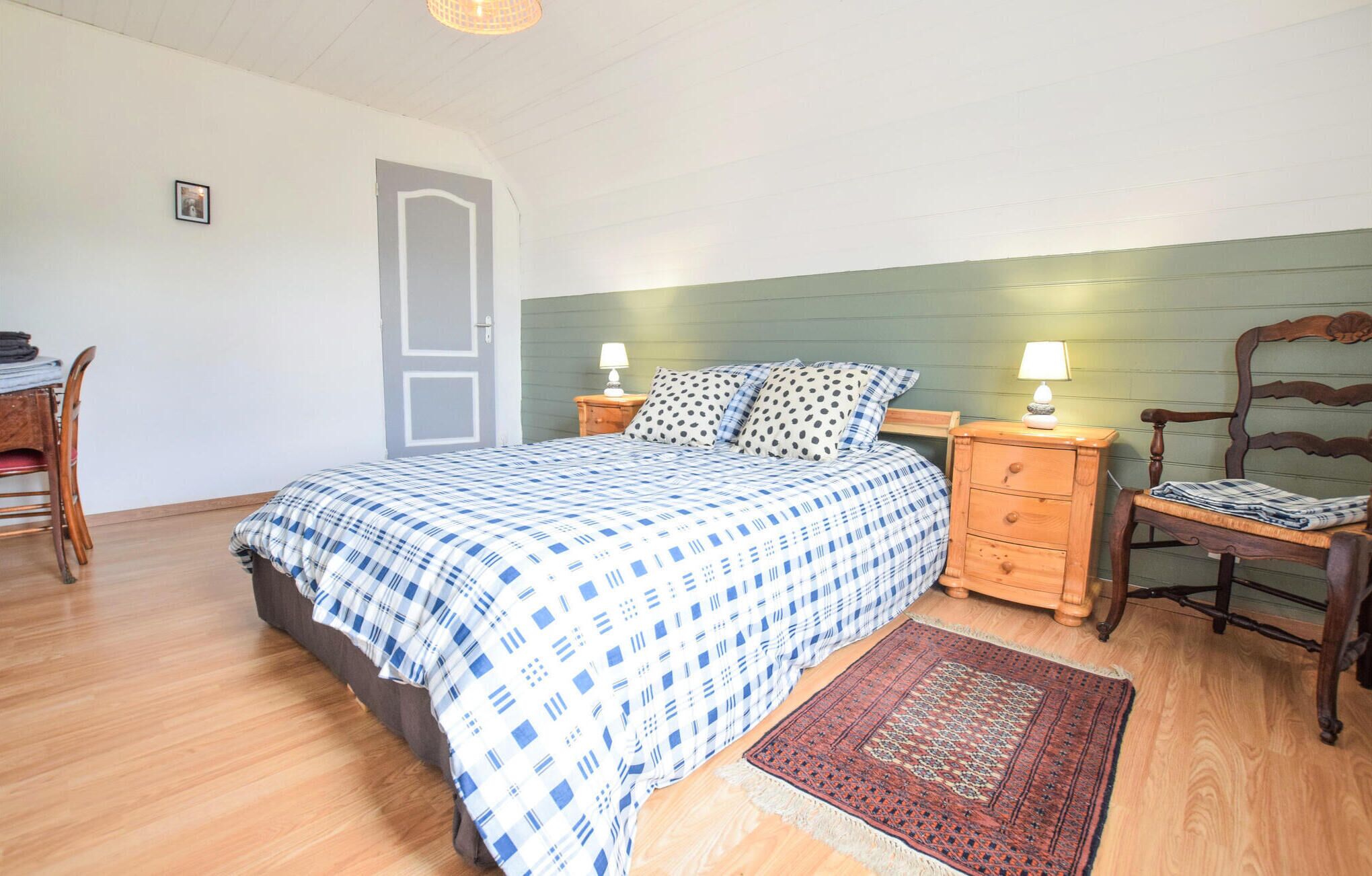 Un dormitorio con una cama, dos mesitas de noche, una silla, un escritorio de madera y una puerta.