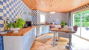 A kitchen with blue and white checkered tiles, wooden ceiling, and a large window offering a view of greenery.