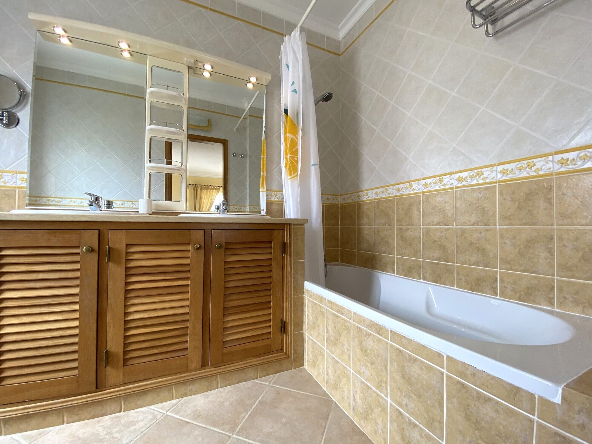Une salle de bain avec un meuble-lavabo en bois, un grand miroir, une baignoire et des murs recouverts de carreaux beiges.