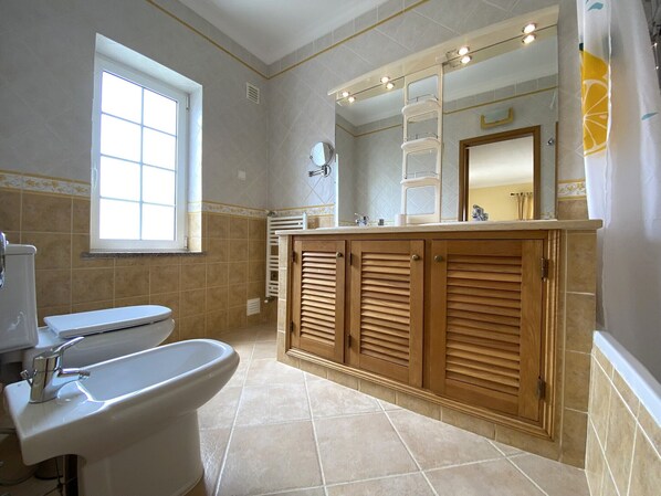 Une salle de bain équipée de toilettes, d’un bidet et d’un meuble-lavabo avec un miroir et des étagères.