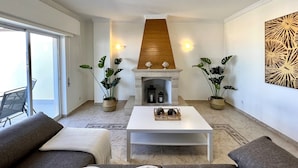 Ein Wohnzimmer mit Kamin, zwei Blumentöpfen, einem weißen Couchtisch und einem Sofa.