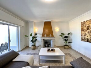 Ein Wohnzimmer mit Kamin, zwei Blumentöpfen, einem weißen Couchtisch und einem Sofa.