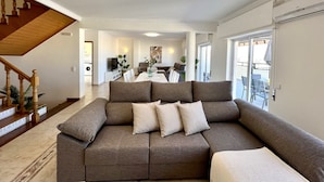 Ein modernes Wohnzimmer mit einer Eckcouch, einem Essbereich und einer Treppe.