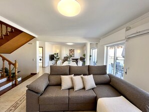 Ein modernes Wohnzimmer mit einer Eckcouch, einem Essbereich und einer Treppe.