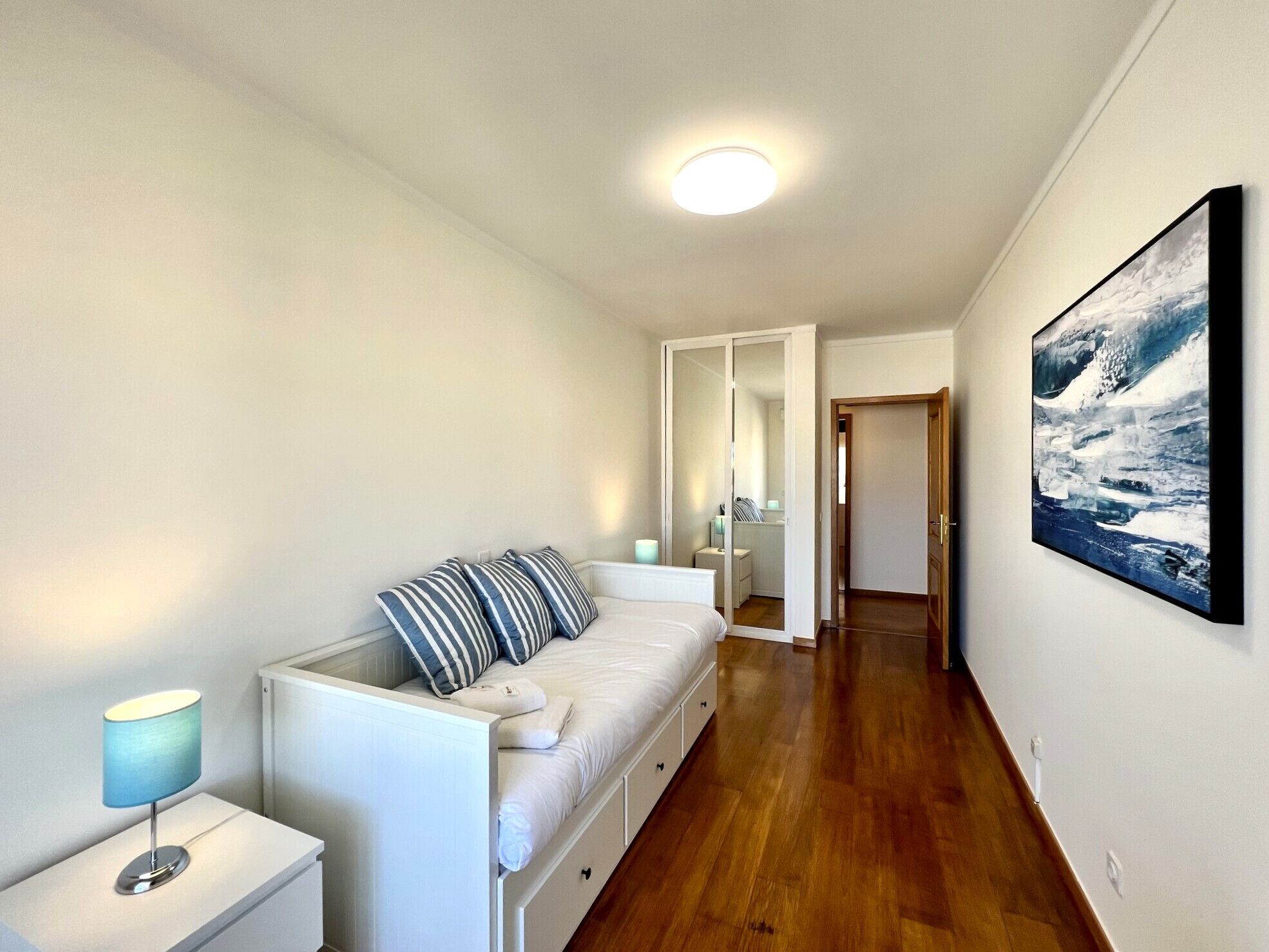 A bedroom with a bed, bedside table, and a painting on the wall.