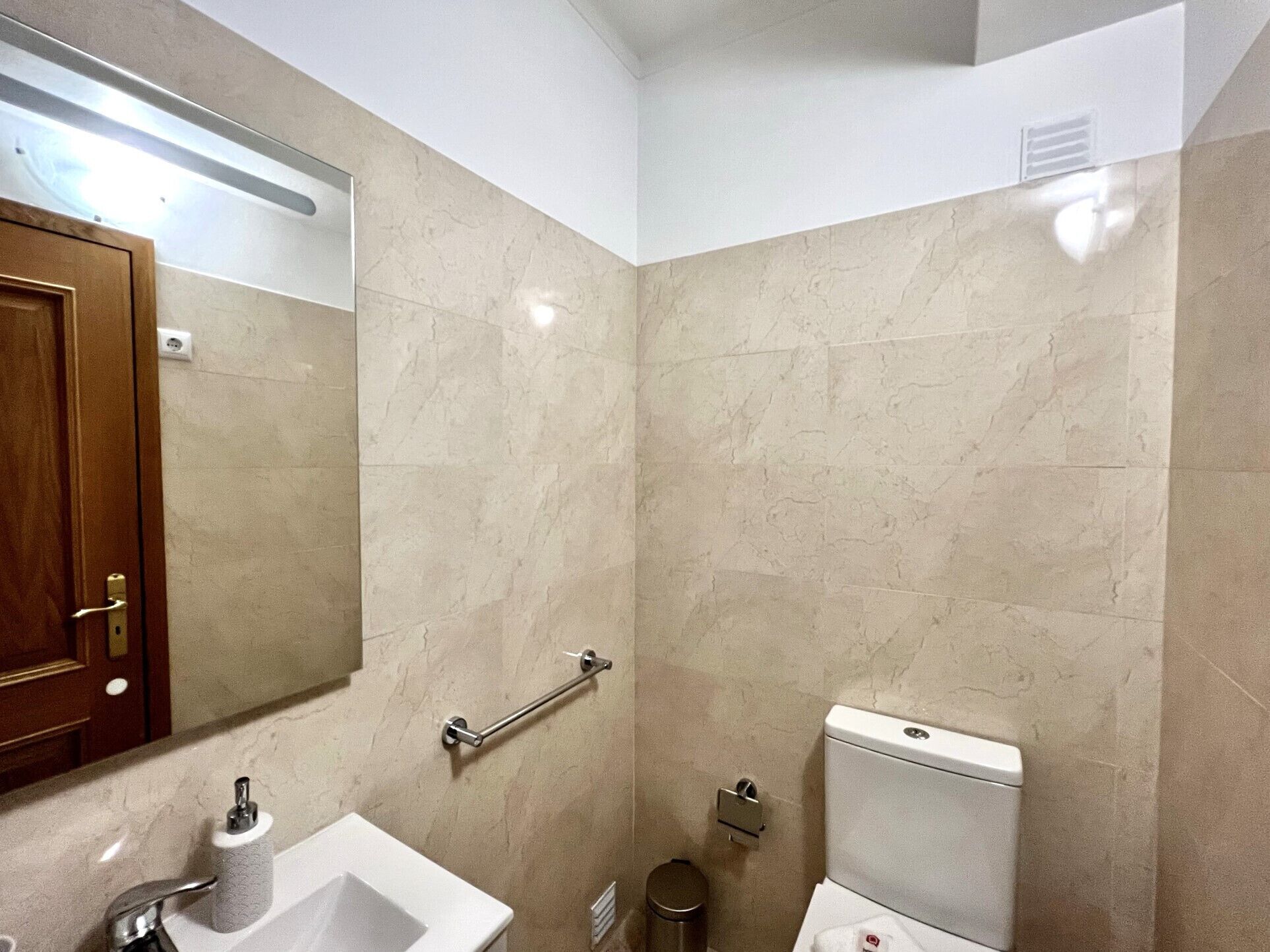 Een badkamer met een wastafel, spiegel, toilet en handgreep.