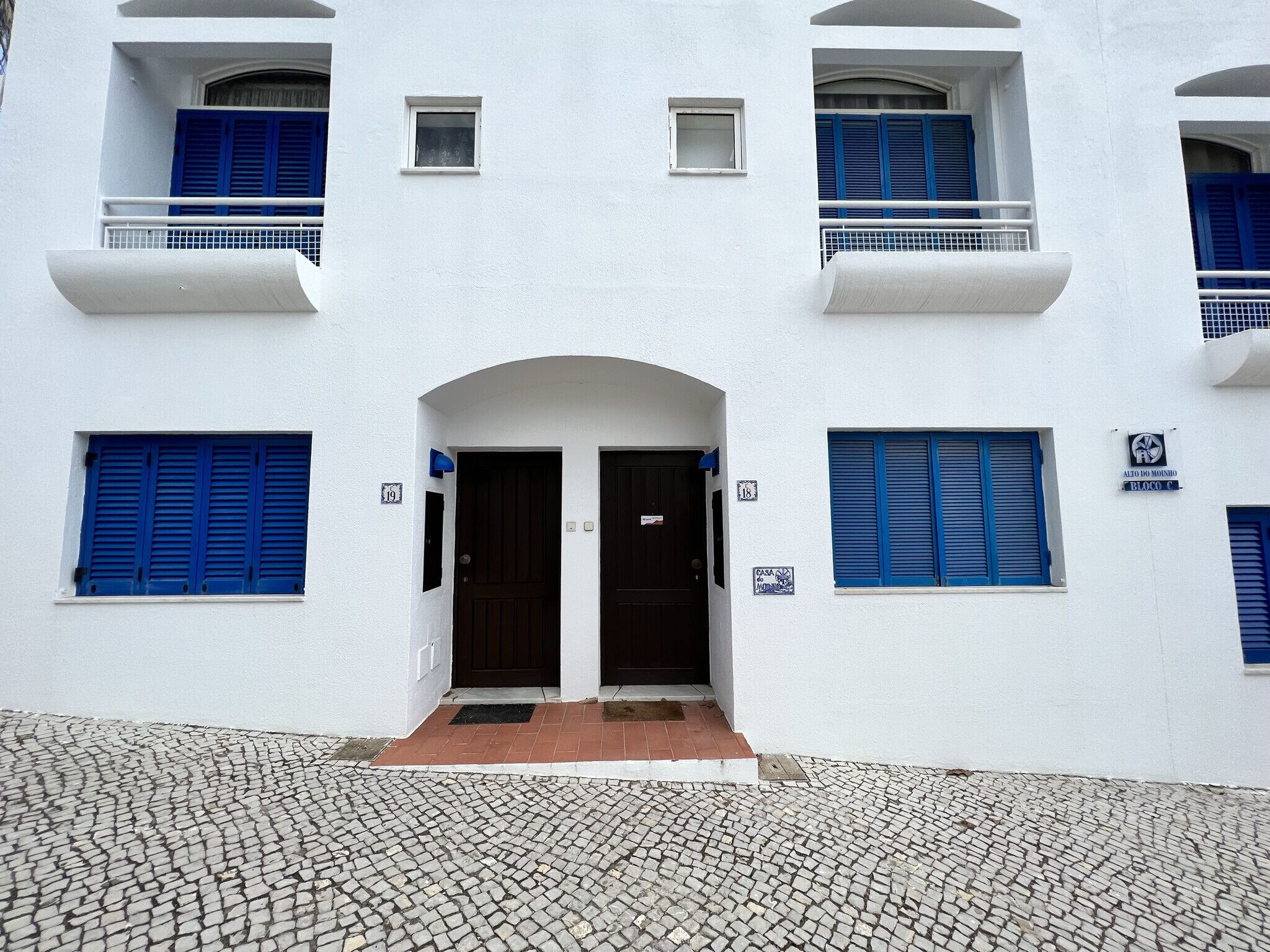 Ein weißes Gebäude mit blauen Fensterläden und einem zentralen Eingang.