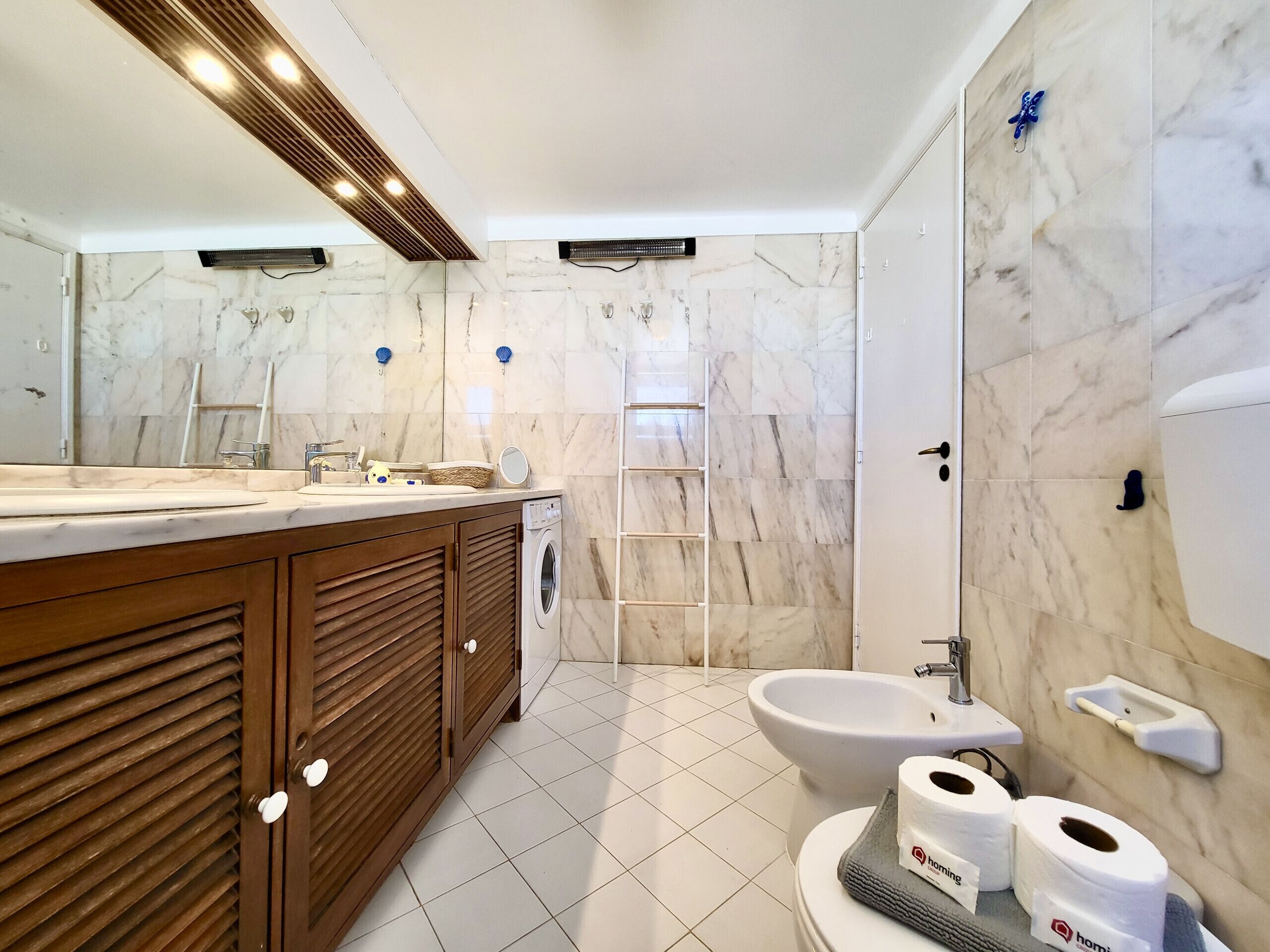 Un baño moderno con salpicadero de mármol, tocador de madera, un bidé y un inodoro con papel higiénico.