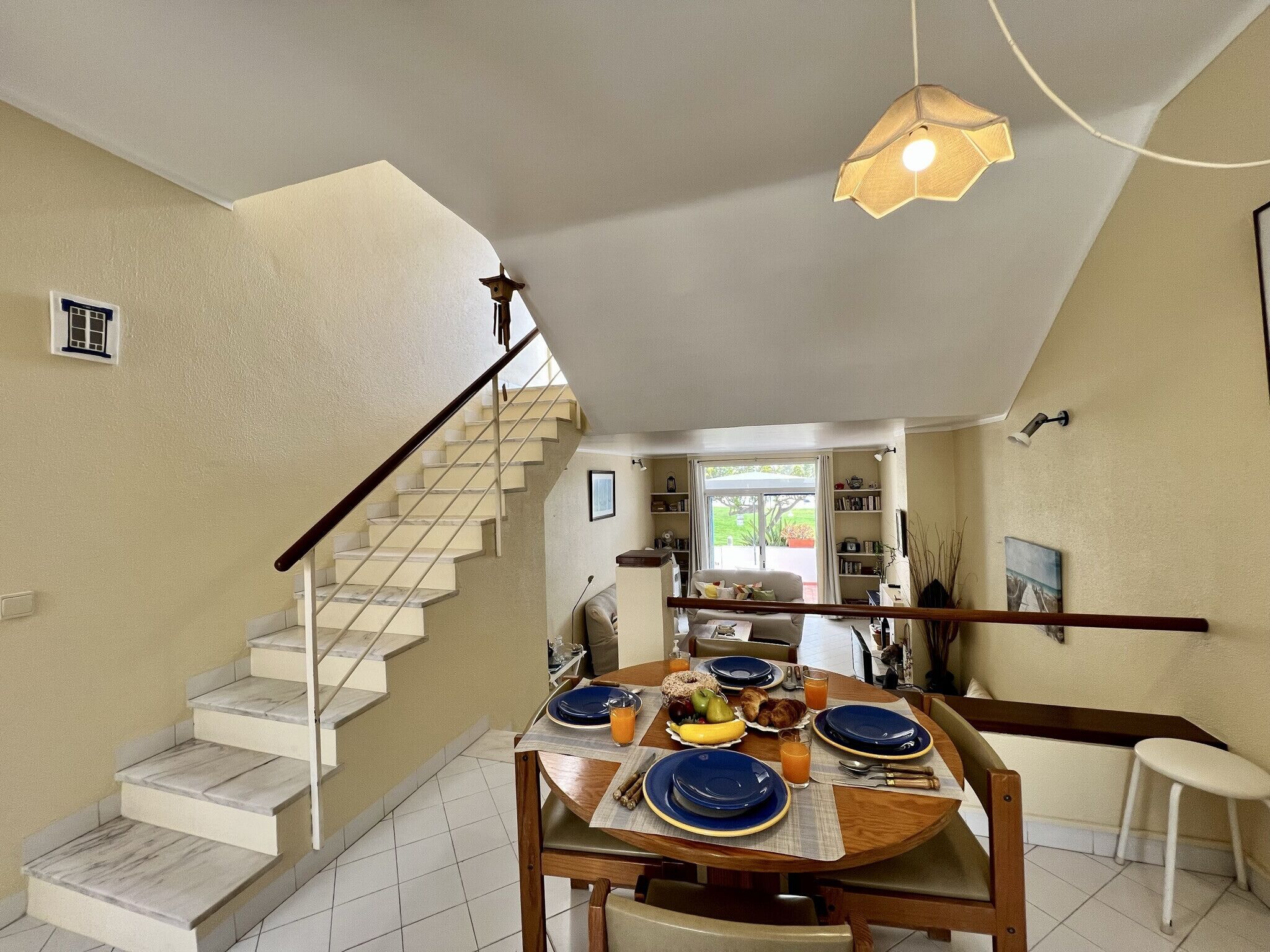 A dining area with a wooden table set for four, a staircase, and a view of the outside.