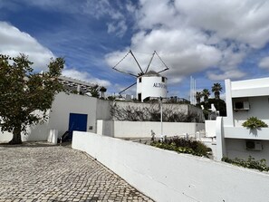 A building with a white facade, a blue door, and a cylindrical structure labeled "ALTO DOME" in the background. - Albufeira Sunset With Pool by Homing (Albufeira)