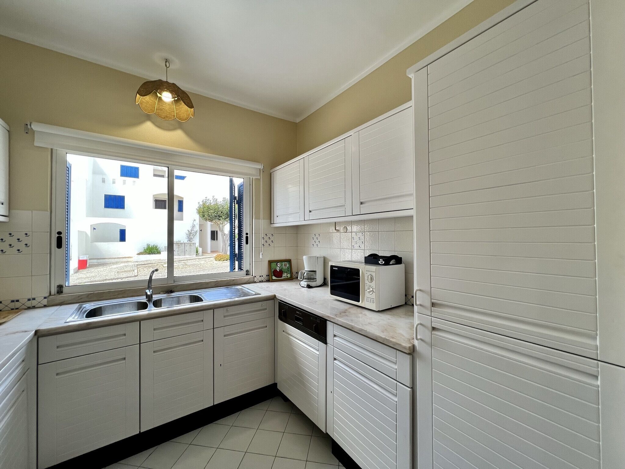 A kitchen with white cabinets, a sink, a window with a view of buildings, and a microwave.