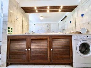 A modern bathroom with a marble vanity, wooden cabinets, a built-in washing machine, and a large mirror. - Albufeira Sunset With Pool by Homing (Albufeira)