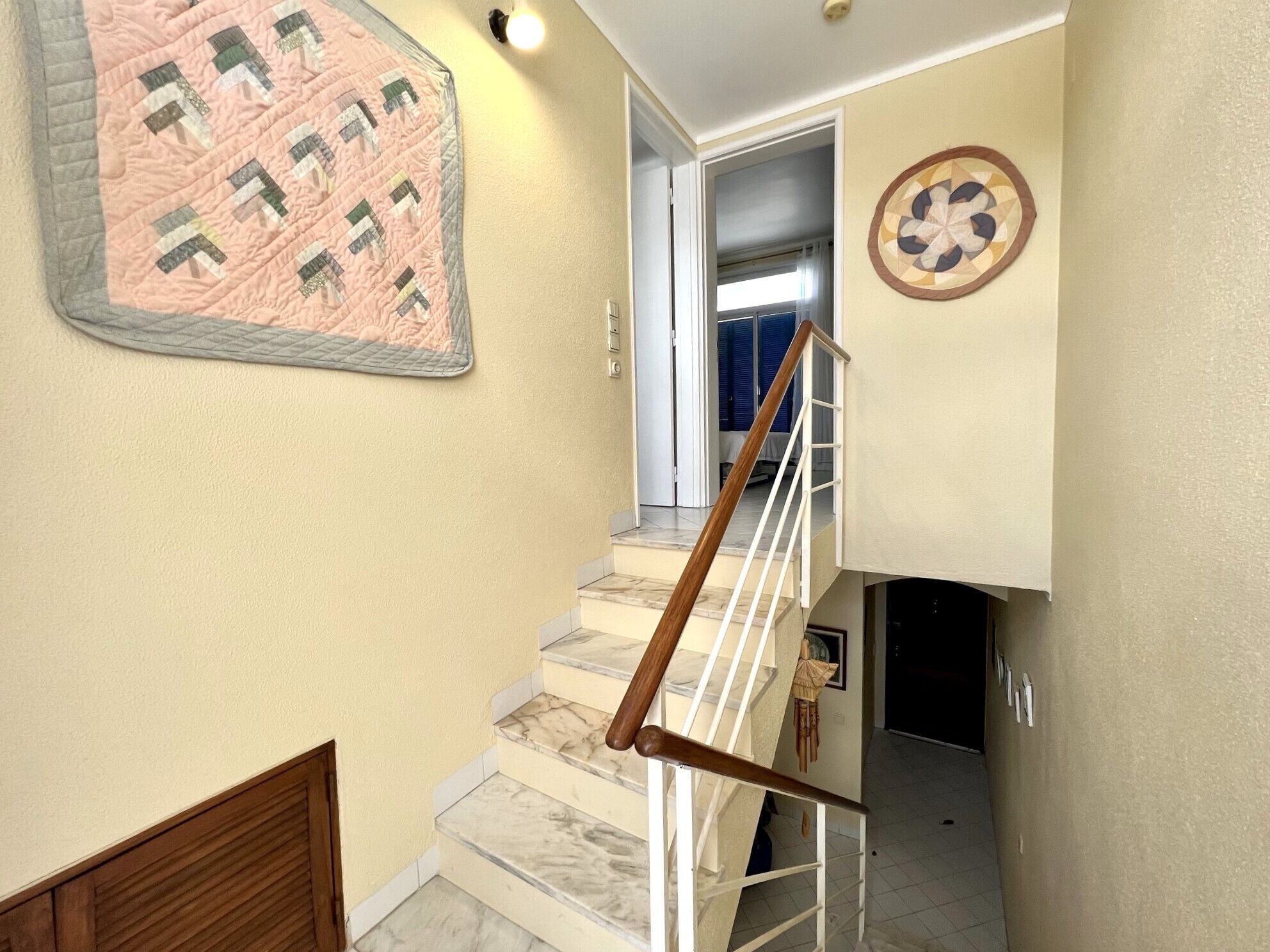 Una escalera con barandilla de madera, un colcha colgada en la pared y un adorno circular en la pared.
