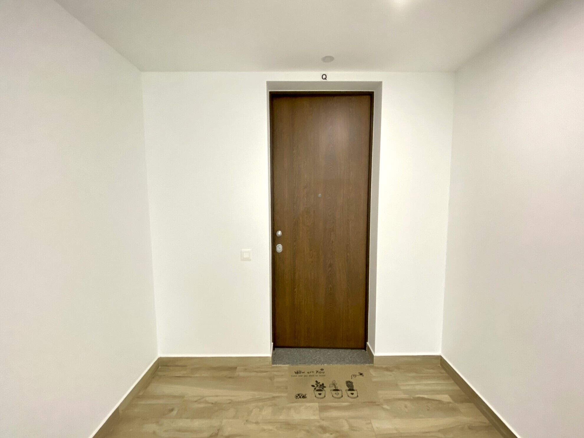 A plain room with a wooden door, white walls, and a wooden floor.