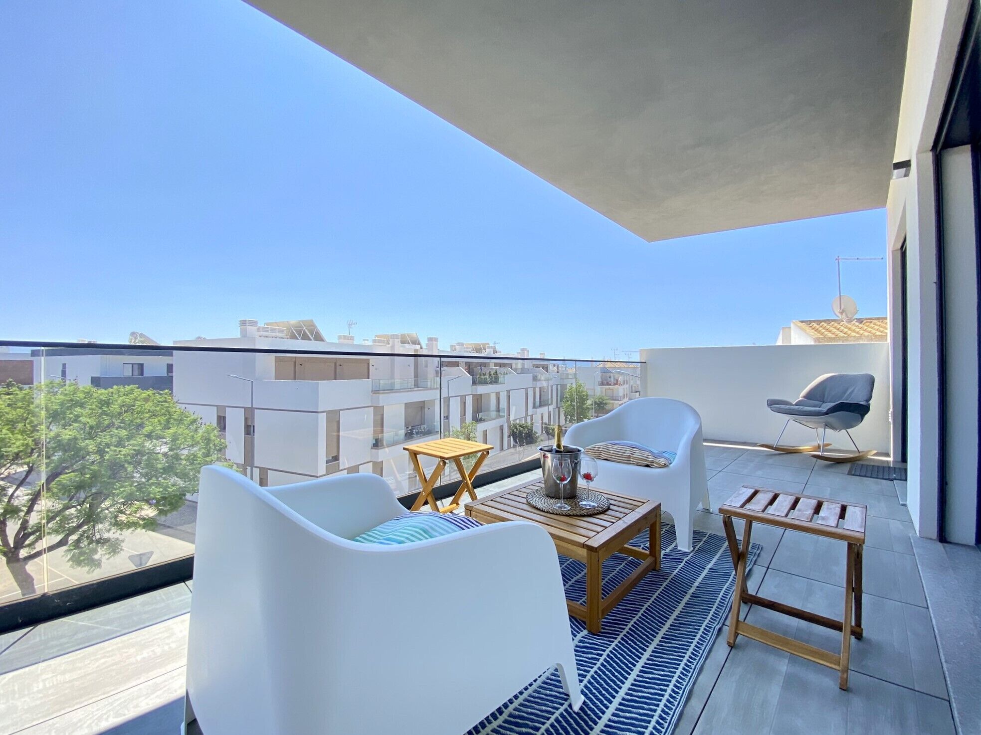 Een balkon met wit meubilair, een klein tafeltje en uitzicht op de stadsgezicht.