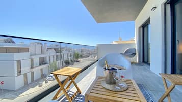 Ein Balkon mit Holztisch, zwei Stühlen, einer Champagnerflasche und Blick auf die Stadt.