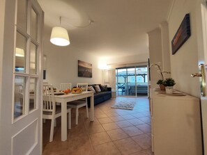A dining area with a white table, chairs, and a breakfast setup. There is a blue sofa and a large window with a view of the outside.