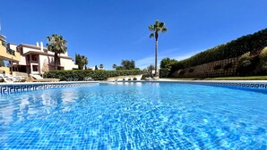 A clear blue swimming pool with tiled edges, surrounded by lounge chairs and palm trees, with buildings in the background. - Albufeira Valley 2 With Pool by Homing (Albufeira)