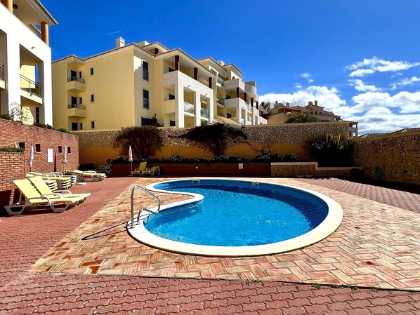 A swimming pool with a brick deck, surrounded by lounge chairs and a stone wall.