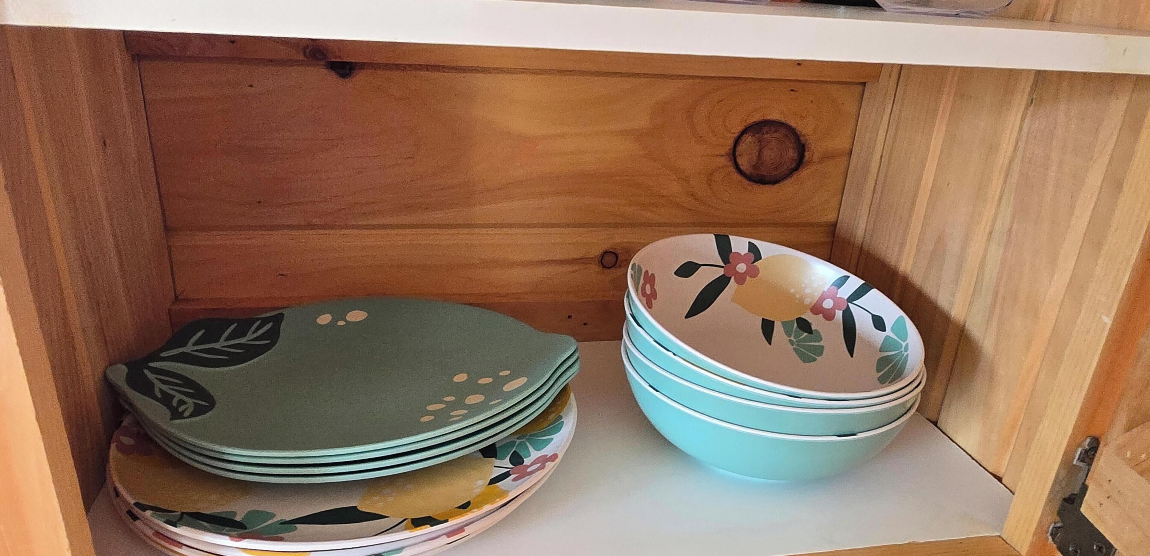 A wooden cabinet with a drawer containing neatly stacked plates and bowls.