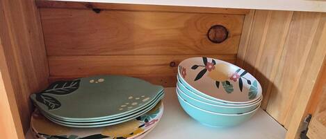 A wooden cabinet with a drawer containing neatly stacked plates and bowls.