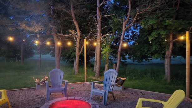 A fire pit surrounded by Adirondack chairs, with string lights overhead.