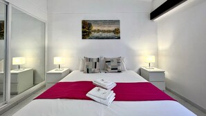 Ett modernt hotellrum med en stor säng, två sängbord med lampor, en tavla på väggen och en röd pläd på sängen.