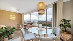 A modern living room with a glass table, wicker chairs, and a large window offering a city view. - Apartamentos Alcazar Oviedo byHOUSY HOST (Medellín)
