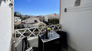 En balkon med et bord og stole, der udover et boligområde med hvide bygninger og en klar blå himmel.