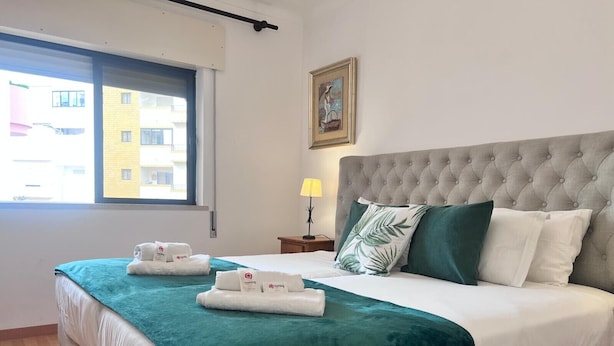 Et hotelværelse med en stor seng, et vindue med udsigt til bygninger, et natbord med lampe og et maleri på væggen.