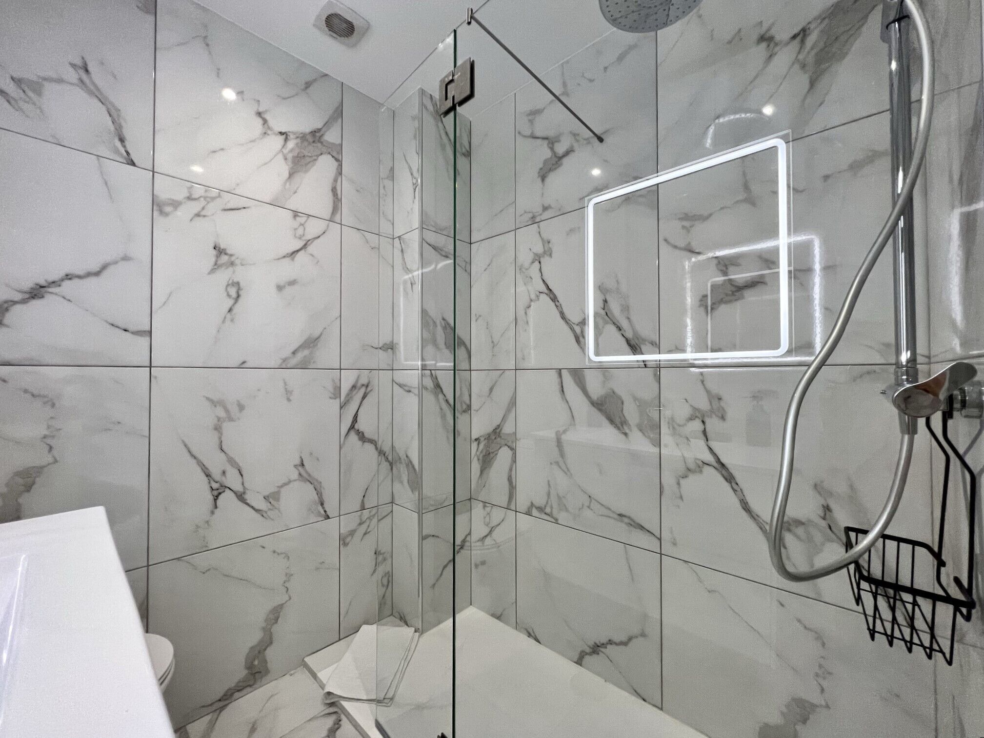 Ein modernes Badezimmer mit Marmorfliesen, einer Duschkabine aus Glas und einer sichtbaren Bedienkonsole für die Dusche.
