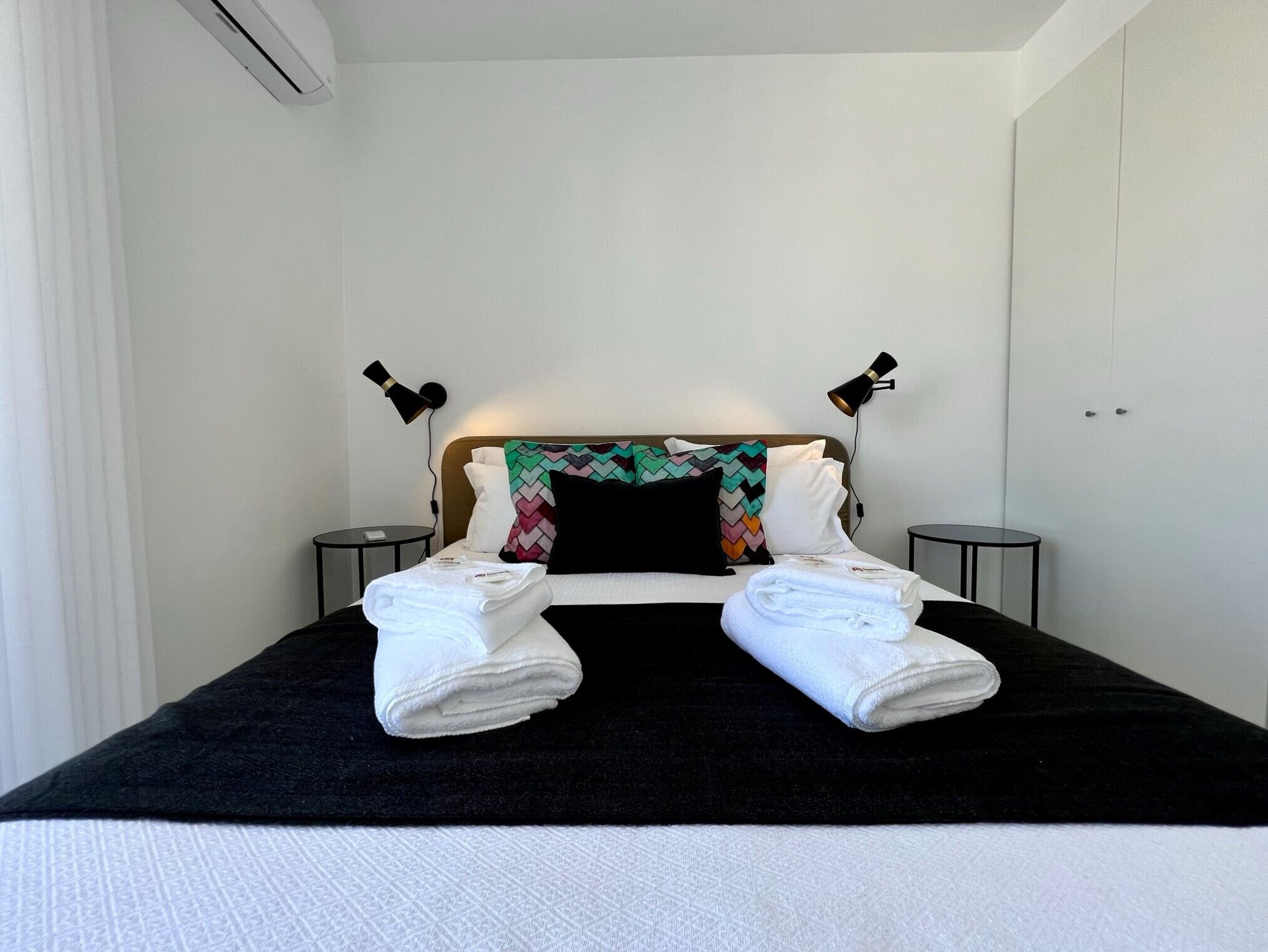 Un lit bien fait, avec du linge de lit blanc, une tête de lit noire et blanche et deux lampes de chevet.