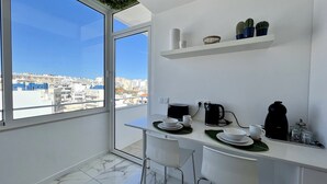 A modern kitchen with a large window, white countertops, and a city view. - Faro Deluxe by Homing (Faro)