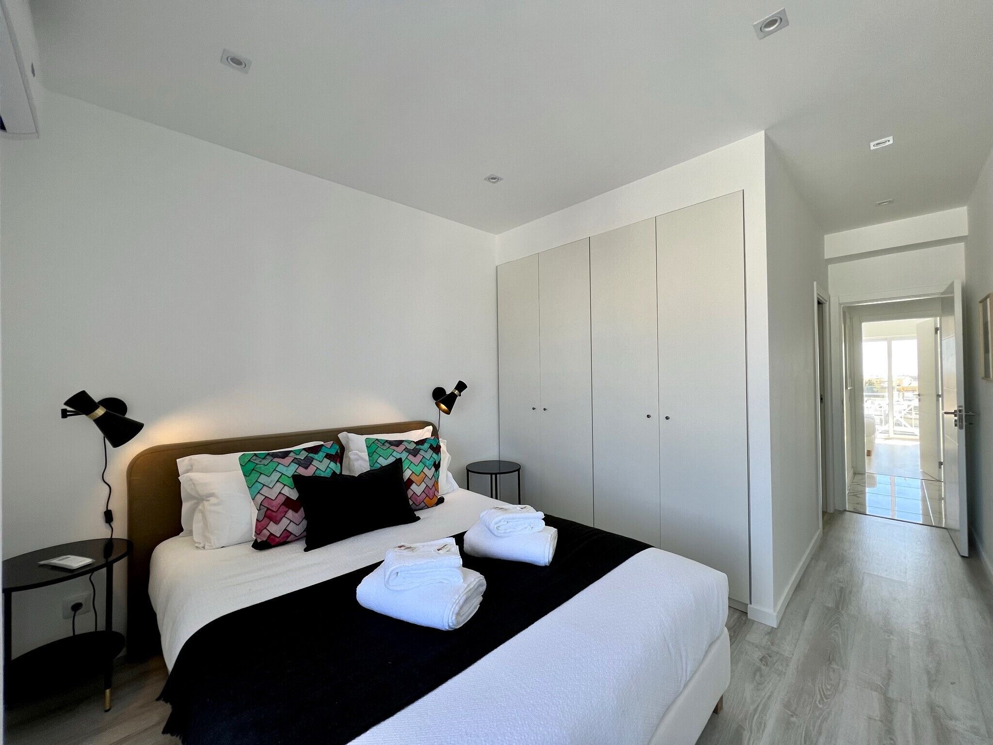 Een moderne hotelkamer met een groot bed, een kledingkast, een nachtkastje en een lamp.